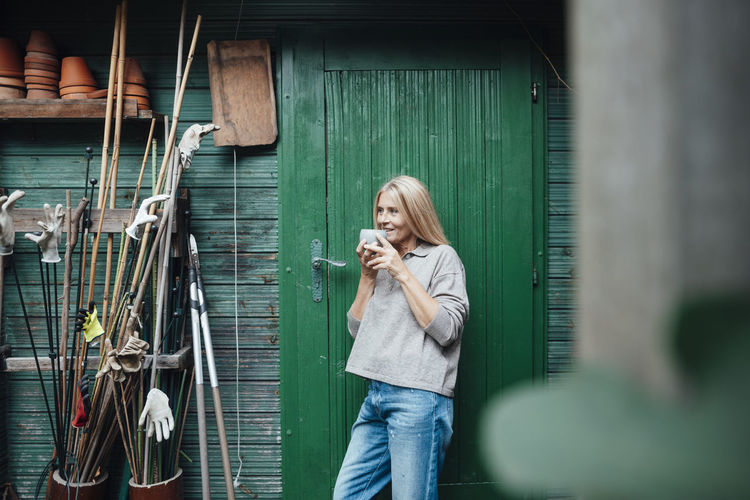 Woman drinking coffee at garden shed entrance