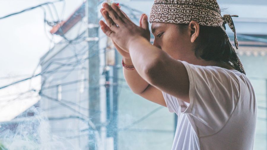 Side view of man praying while standing against building