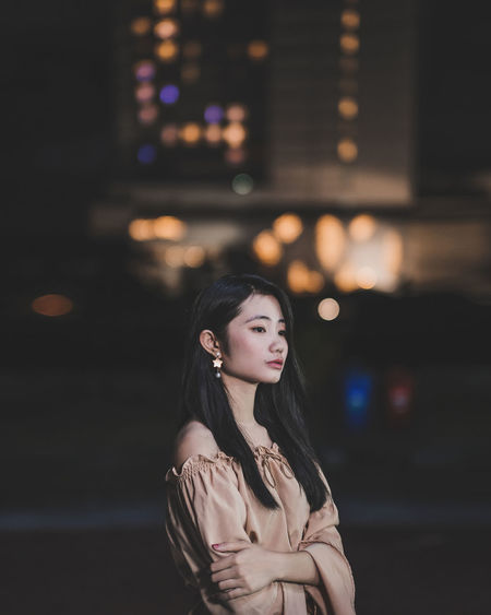 Young woman looking away while standing outdoors at night