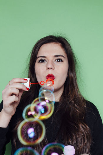 Portrait of young woman blowing bubbles against green background