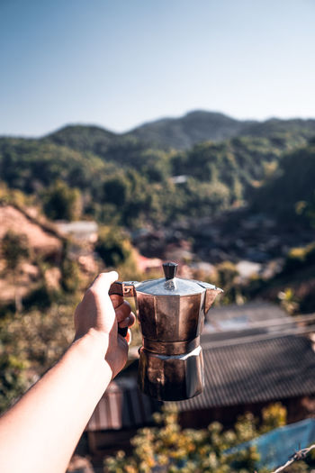 Close-up of hand holding coffee cup against mountain range