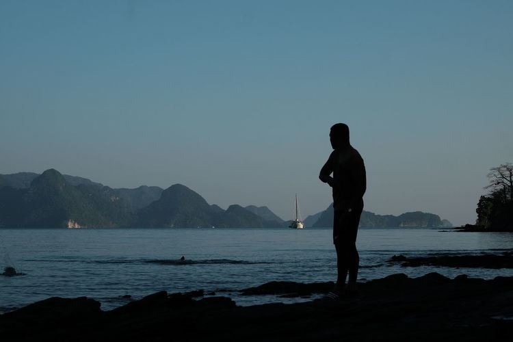 Silhouette man standing by lake against clear sky
