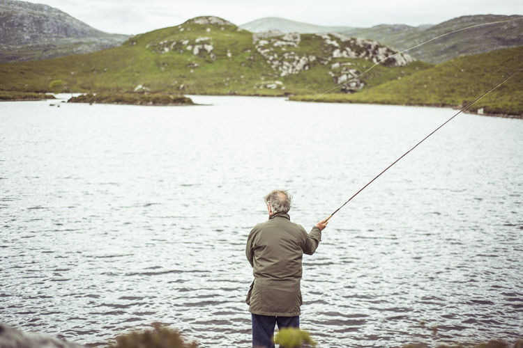 Man fly fishing by loch in remote mountains in scotland
