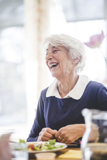 Cheerful senior woman having lunch at table in nursing home