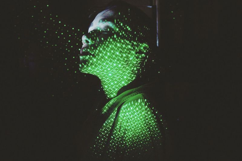 Close-up of shirtless woman with illuminated green lights against black background