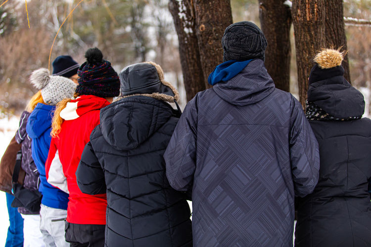 Rear view of people standing by tree outdoors during winter
