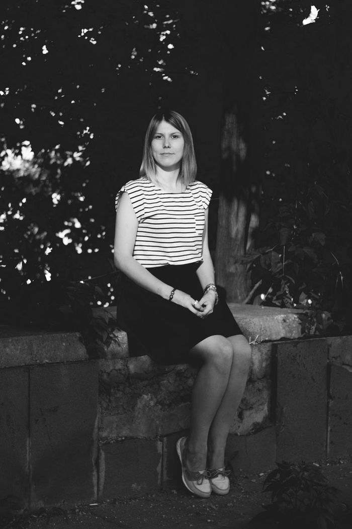 Full length portrait of young woman sitting on retaining wall against trees