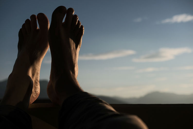 Low section of man with feet up against sky