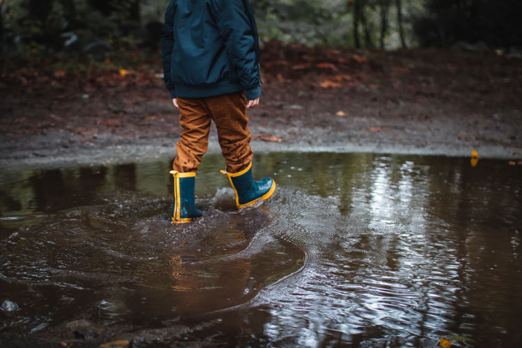 Low section of boy wearing boots while walking in puddle in forest
