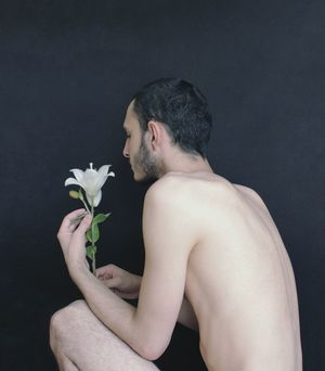 MIDSECTION OF SHIRTLESS MAN HOLDING ROSE IN BLACK BACKGROUND