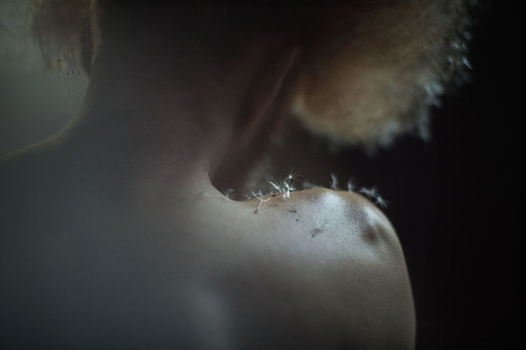 Close-up of dandelion seeds on woman shoulder in darkroom