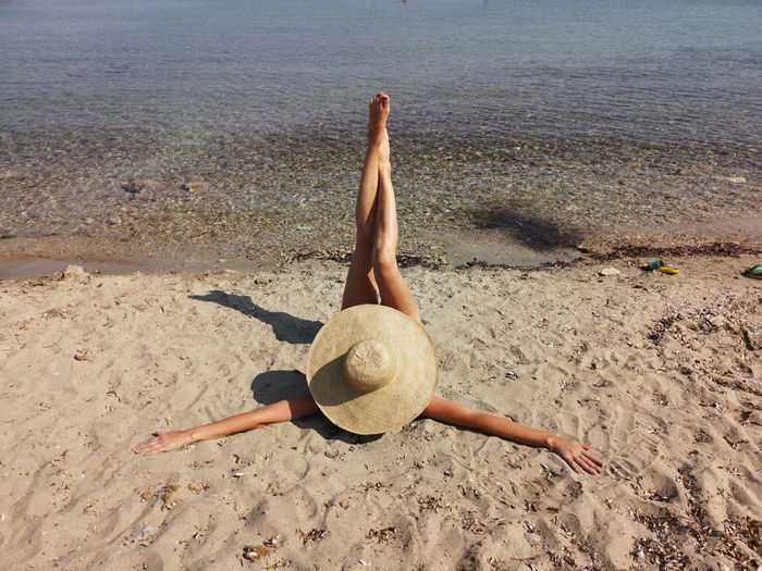 Mature woman lying on a sand beach her head covered with hat