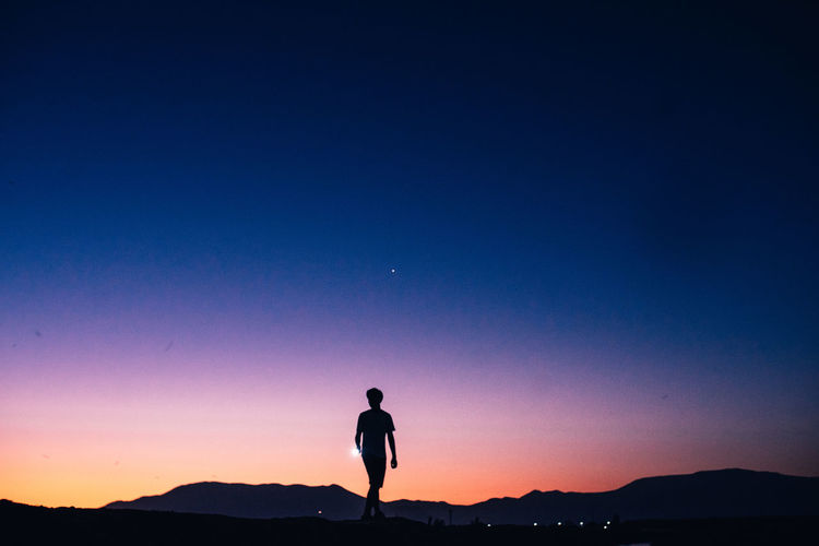Silhouette man standing on mountain against clear sky during sunset