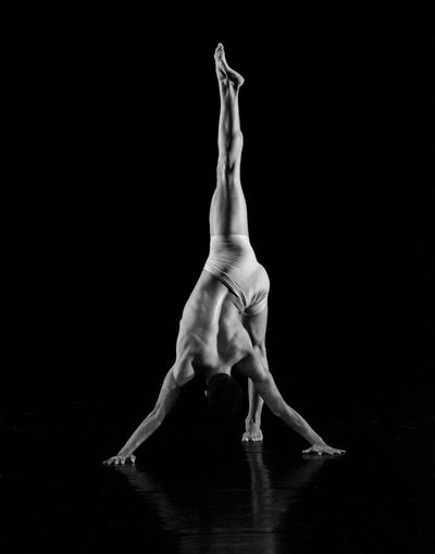 Full length of shirtless dancer performing against black background