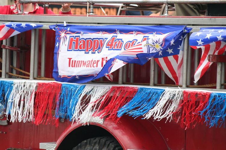 Banner with text on vehicle trailer over street during fourth of july parade
