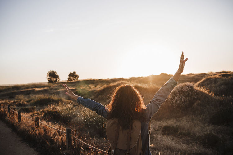 Carefree woman standing with arms raised in nature during sunset