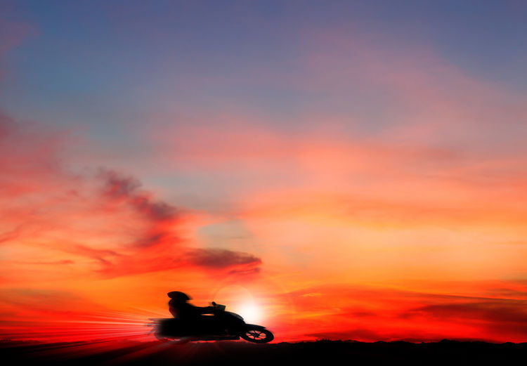 Silhouette person riding bicycle against dramatic sky during sunset