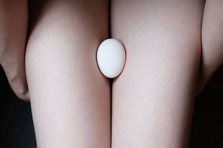 Midsection of naked woman holding egg against black background