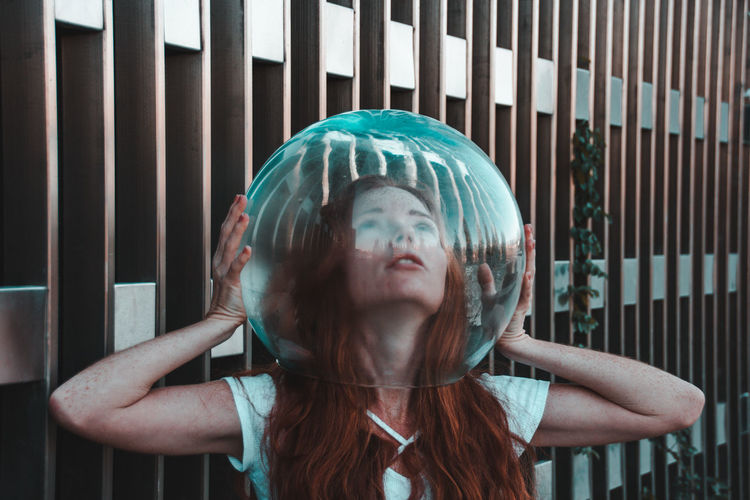 Close-up of young woman removing glass helmet from head against metallic railing