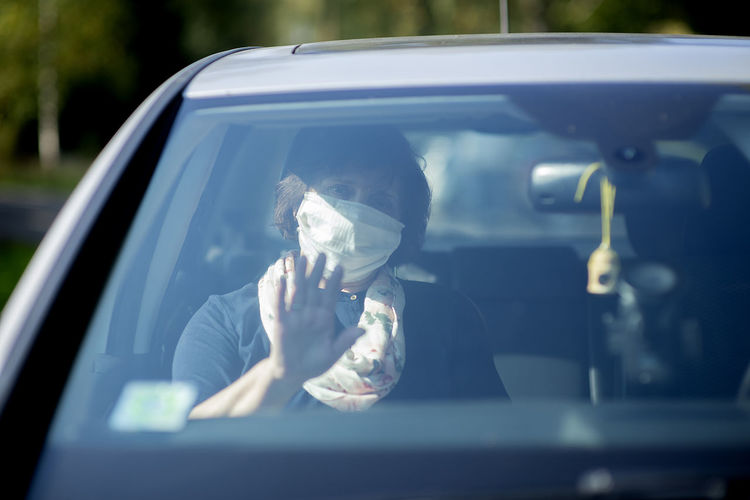 Elderly senior woman wearing a face mask while sitting in car during covid-19 epidemic