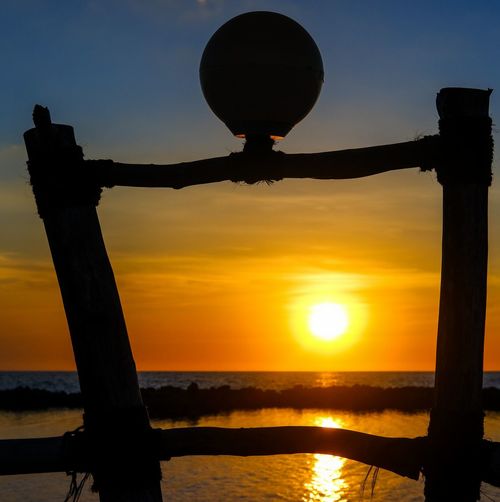 Silhouette wooden post on beach against sky during sunset