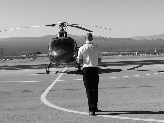 Rear view of pilot standing by helicopter at helipad