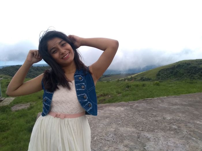 Portrait of smiling teenage girl standing on mountain against sky