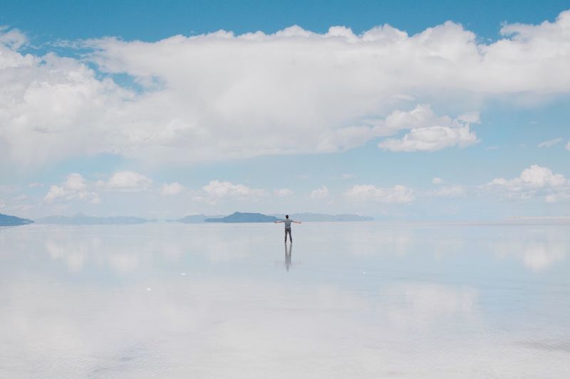 Man with arms outstretched standing on salt flat against cloudy sky