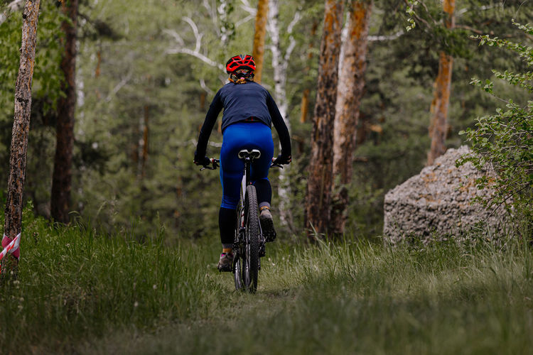Back woman riding mountain bike on forest trail