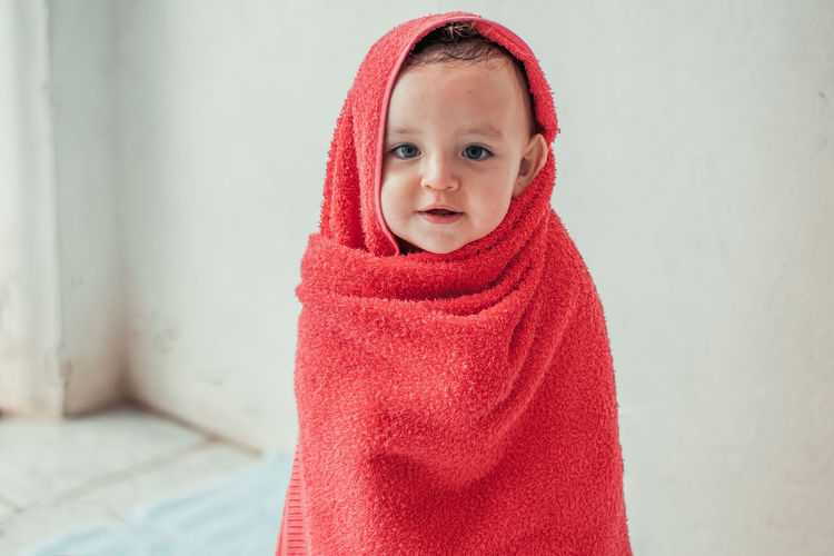 Portrait of cute boy wrapped in red towel at home