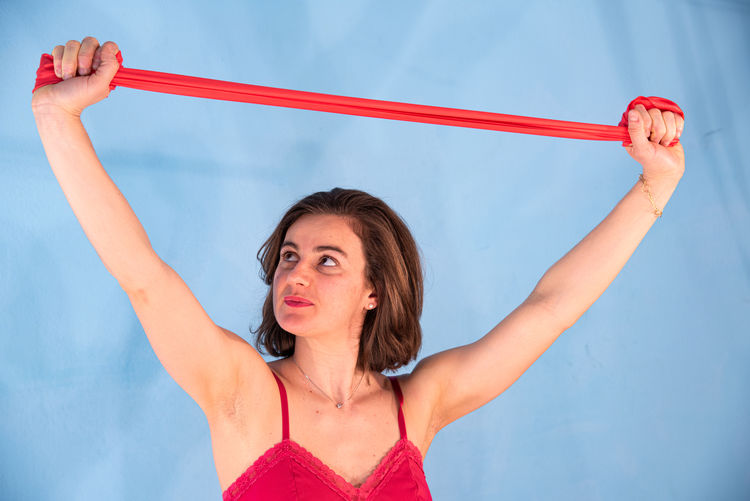 Woman holding red resistance band against blue wall