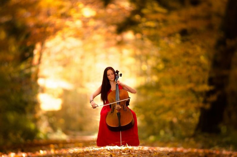 Beautiful woman playing double bass in forest during autumn
