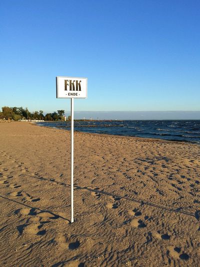 Information sign on beach against clear blue sky