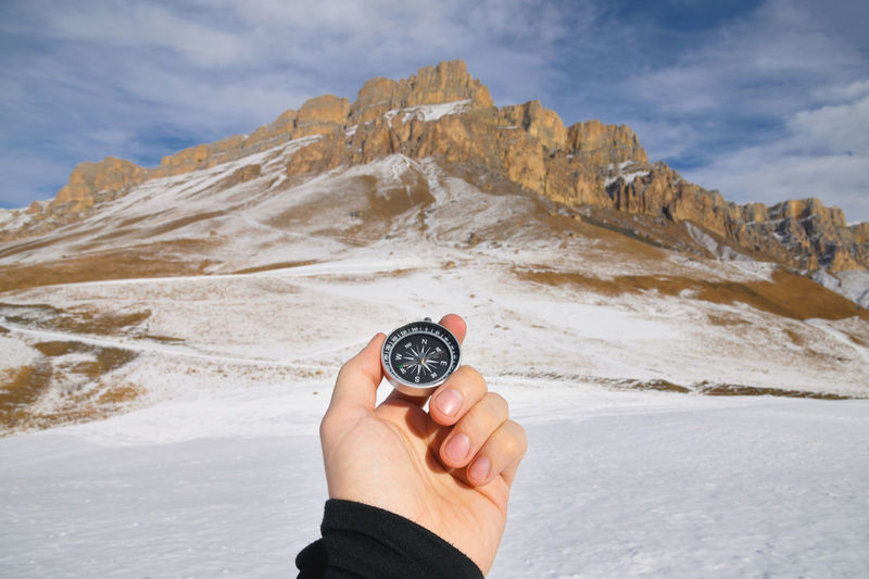 A man s hand holds a pocket magnetic compass for navigation against the backdrop of winter rocky 