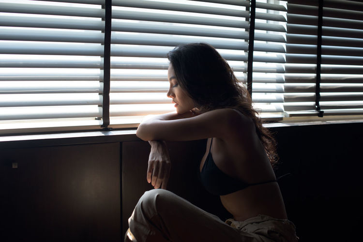 Young woman sitting by blinds at home