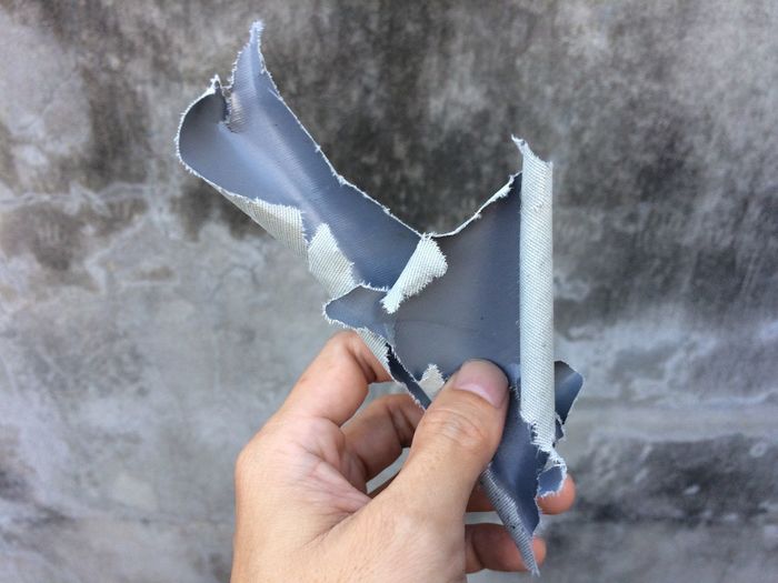 Cropped hand holding duct tape by wall