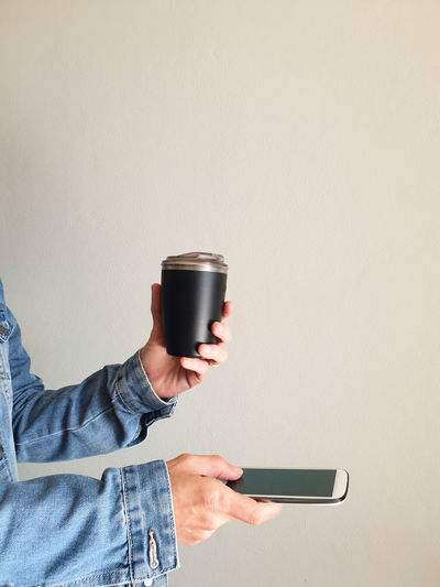 Cropped female hand holding reusable coffee cup and smartphone