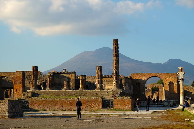 People on old ruin of pompeii against sky with volcano vesuvius in background