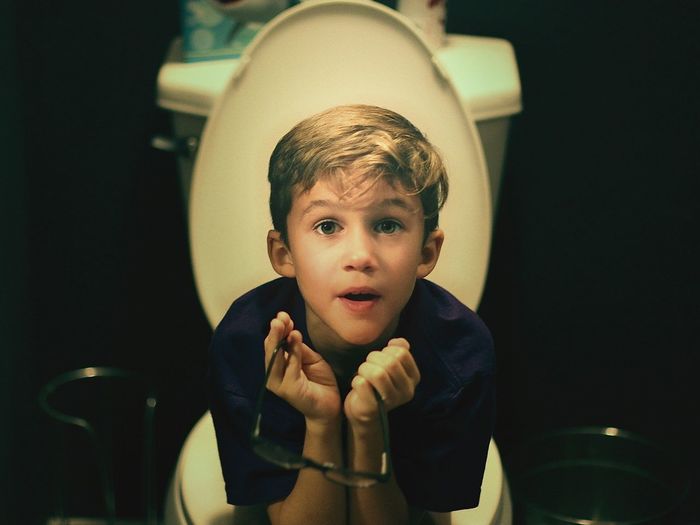 Portrait of boy sitting on toilet bowl in bathroom