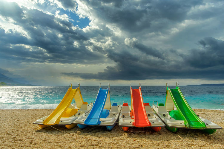 Deck chairs on beach against cloudy sky