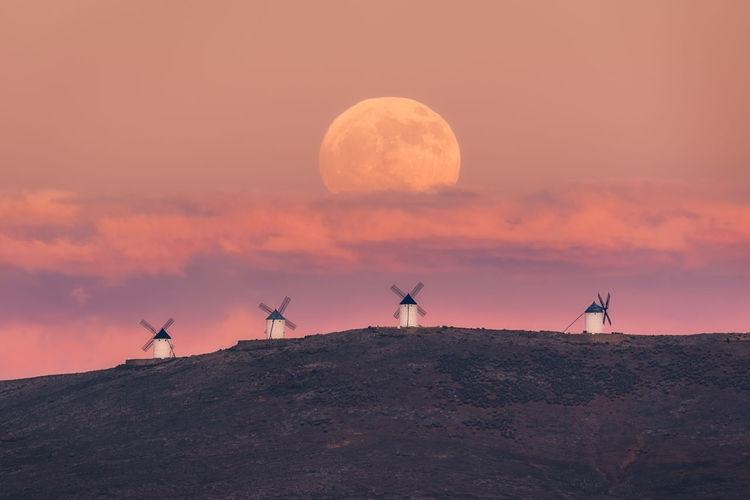 Amazing scenery of majestic full moon over valley with windmills in sundown