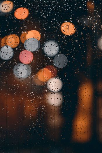 Full frame shot of raindrops on window against defocused lights