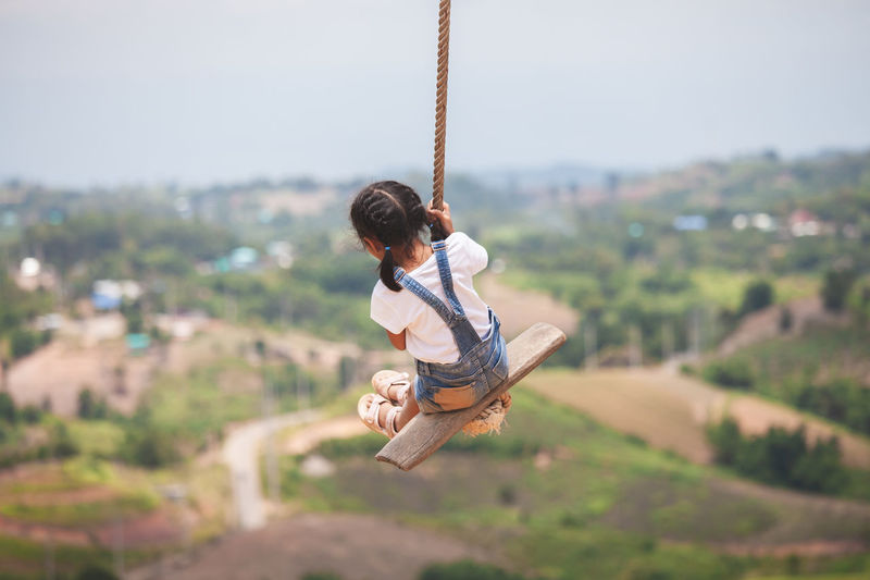 Full length of girl swinging against landscape