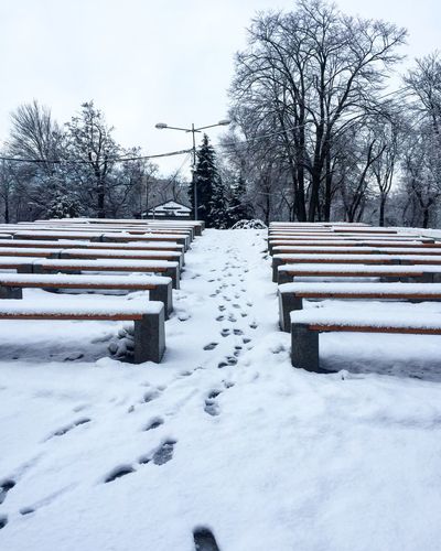 Snow covered bench on field against sky