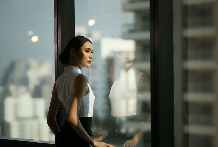 Businesswoman looking away while standing by window at office