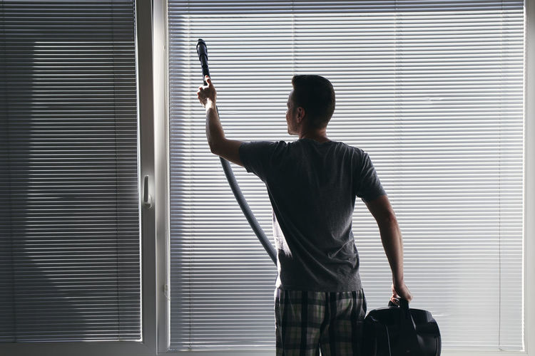 Rear view of man cleaning window at home