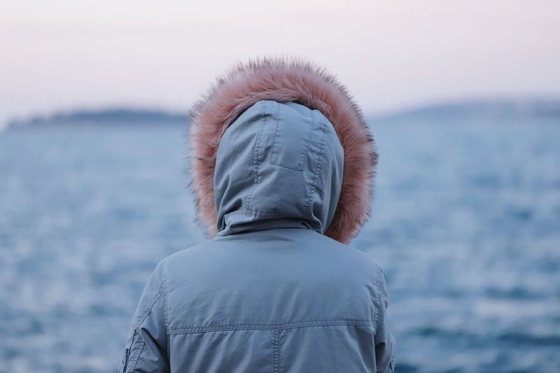 Rear view of woman looking at sea against sky during winter