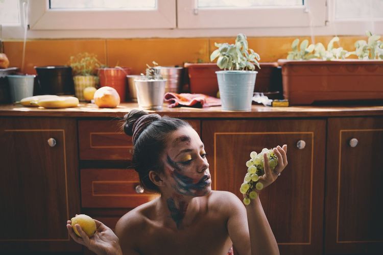 Woman with face paint holding fruits in kitchen