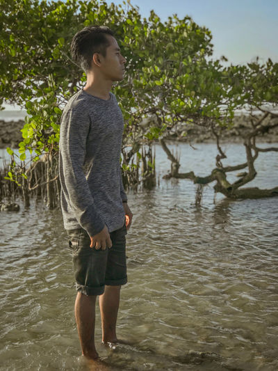 Full length of man standing in sea against trees