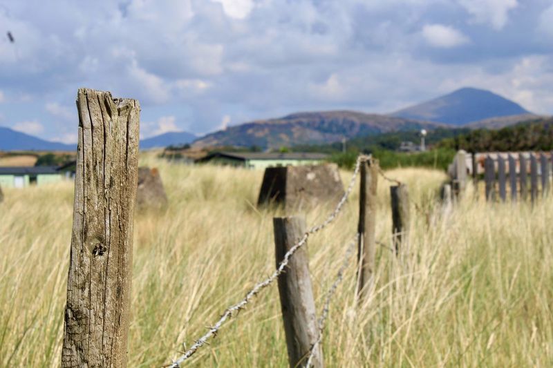 Fence on grassy land against cloudy sky